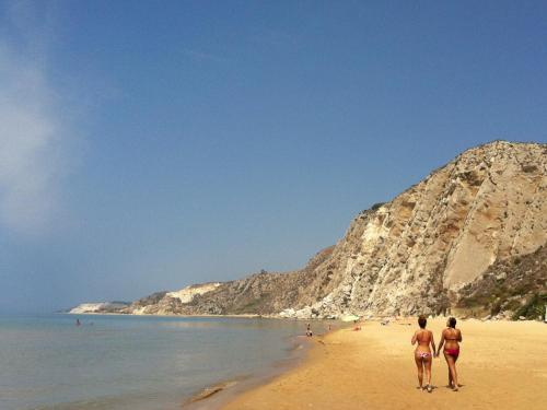 two people walking on a beach with a mountain at Hotel Costazzurra Museum & Spa in San Leone