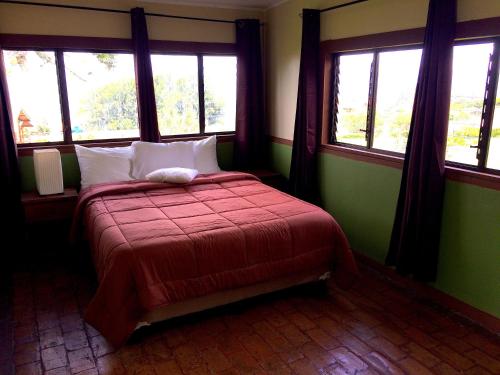 a bedroom with a bed with a red comforter and windows at Grandpas Hotel & Restaurante in Cartago