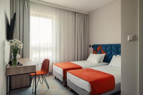 una camera d'albergo con due letti, una scrivania e una finestra di Hotel Faros Gdansk Airport a Danzica Rebiechowo