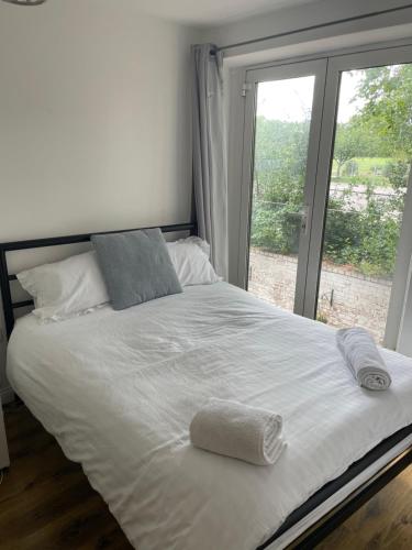 a white bed with two towels on it in front of a window at Mac-Stephneil Holiday Homes in London