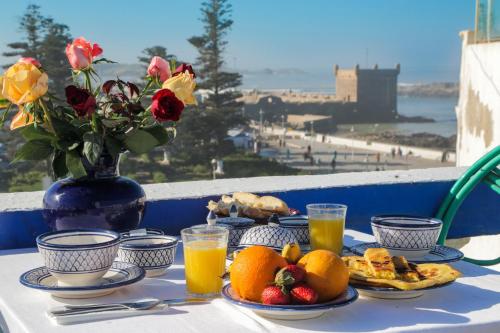 a table with plates of fruit and juice and a vase with flowers at Villa Maroc Essaouira in Essaouira