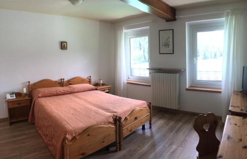 a bedroom with a wooden bed and two windows at Hotel Juventus in Auronzo di Cadore