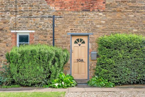 une porte en bois dans un bâtiment en briques avec des buissons dans l'établissement The Limes - Beautiful Townhouse in Oakham, à Oakham