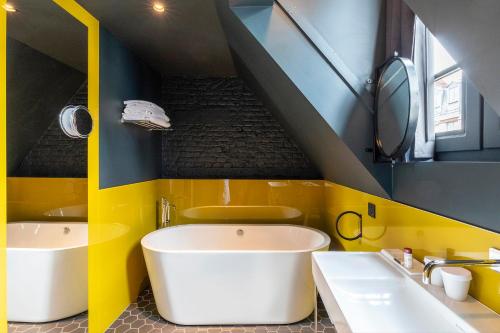 a yellow and blue bathroom with two sinks and a tub at Clarance Hotel Lille in Lille