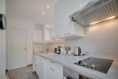 La cuisine est équipée de placards blancs et d'un four avec plaques de cuisson. dans l'établissement Appartement - Cannes vieille ville - Le Suquet, à Cannes