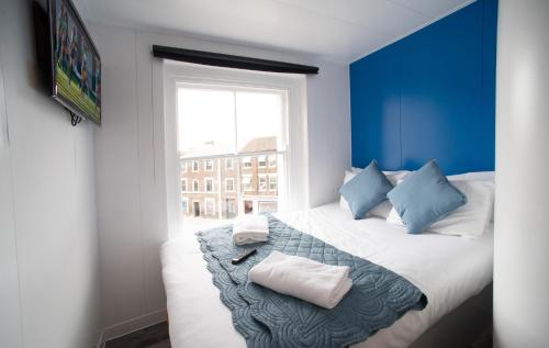 ein blaues Zimmer mit einem Bett mit Kissen und einem Fenster in der Unterkunft CiTi Hotel London Luton in Luton