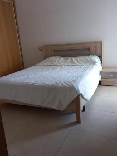 uma cama com lençóis brancos e uma estrutura de madeira num quarto em appartement luxe em Mohammedia