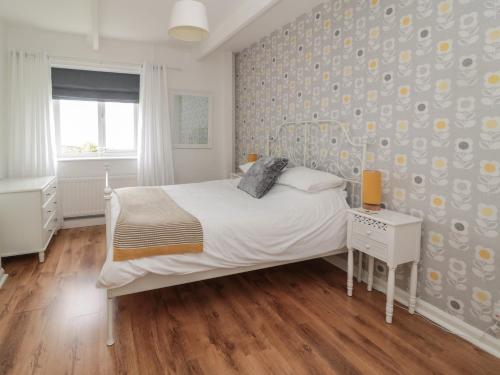 Un dormitorio con una cama blanca y una pared con flores en South Cottage Howick, en Craster