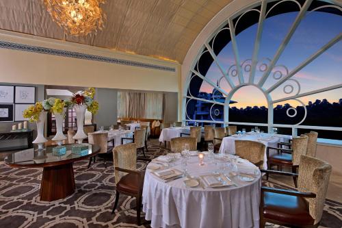 a dining room with tables and chairs and a large window at The Leela Palace Bengaluru in Bengaluru