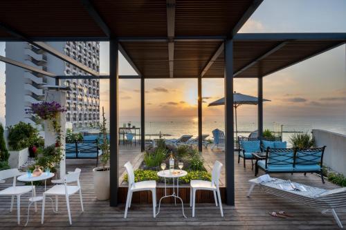 a deck with tables and chairs and the ocean at Maxim Design Hotel 3 Star Superior in Tel Aviv