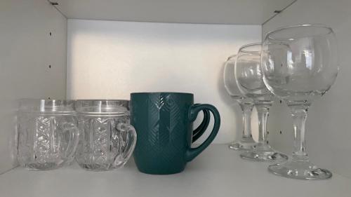 une rangée de verres à vin et une tasse verte sur une étagère dans l'établissement Mini Wind Apartment, à Liepāja