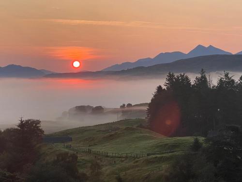 a misty sunrise on a hill with the sun setting at Aspen Lodge in Oban
