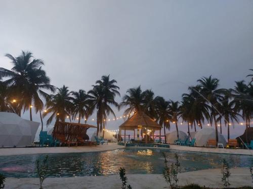 a resort pool with palm trees and a gazebo at Aqua Breeze Glamping in San Bernardo del Viento