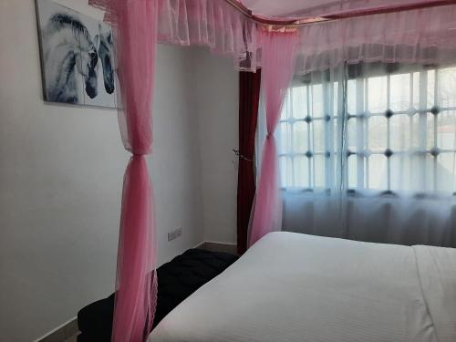 a bedroom with a bed with pink curtains and a window at Deerwood Family Apartments, Bulenga in Bulenga