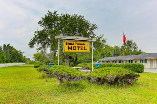 Stone Fountain Motel في Fenelon Falls: علامة على وجود موتيل في حقل مع الشجر