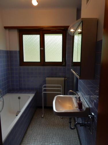 La salle de bains est pourvue de carrelage bleu, d'une baignoire et d'un lavabo. dans l'établissement GITE KIENTZLER, à Ribeauvillé