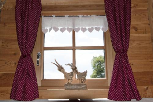 a window with red curtains and a statue of deer in a window sill at Baita dei Fovi in Baselga di Pinè