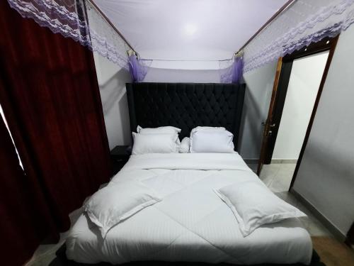 a bed with white sheets and pillows in a room at Deerwood Family Apartments, Bulenga in Bulenga