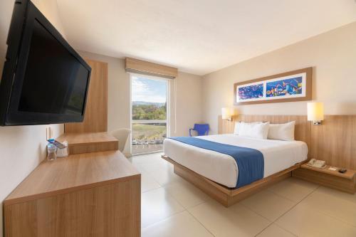 City Express by Marriott San José Costa Rica في سان خوسيه: غرفة فندقية بسرير وتلفزيون بشاشة مسطحة