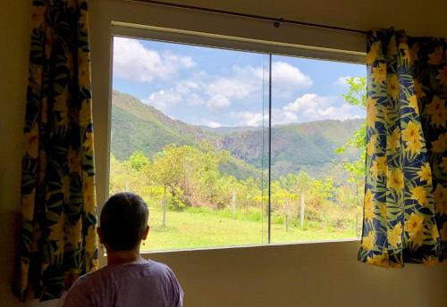 a man looking out a window at a mountain view at Casa do Alecrim in São Roque de Minas