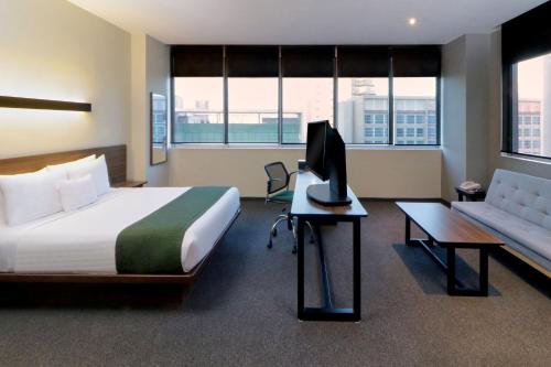 City Express Suites by Marriott Santa Fe في مدينة ميكسيكو: غرفة في الفندق بها سرير وتلفزيون وأريكة
