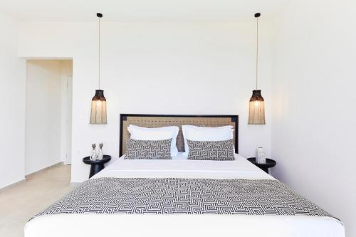 a white bedroom with a large bed with two tables at Skiathos Ammos Luxury Apartments in Skiathos Town