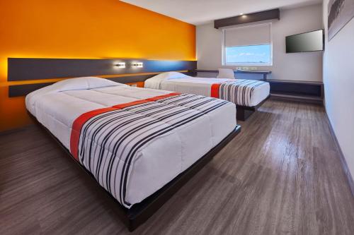 2 Betten in einem Zimmer mit orangefarbenen Wänden in der Unterkunft City Express Junior by Marriott San Luis Potosi Carranza in San Luis Potosí