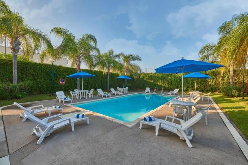 a swimming pool with chairs and blue umbrellas at City Express by Marriott Mazatlan in Mazatlán