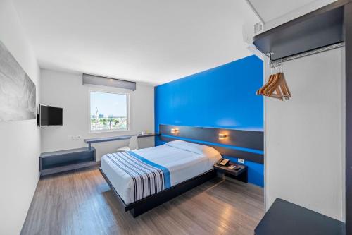 a blue bedroom with a bed and a window at City Express Junior by Marriott Merida Altabrisa in Mérida