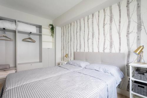 a white bedroom with a bed and a wall with trees at Apartamento tranquilo y céntrico en Santander in Santander