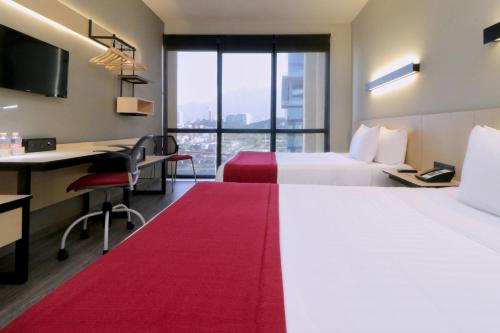 a hotel room with two beds and a desk at City Express Plus by Marriott Monterrey Galerías in Monterrey