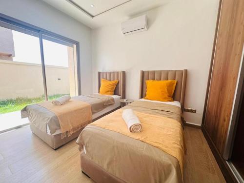 two beds with orange pillows in a room with a window at Villa Dream Oujda Piscine Chauffée sans vis à vis in Oujda