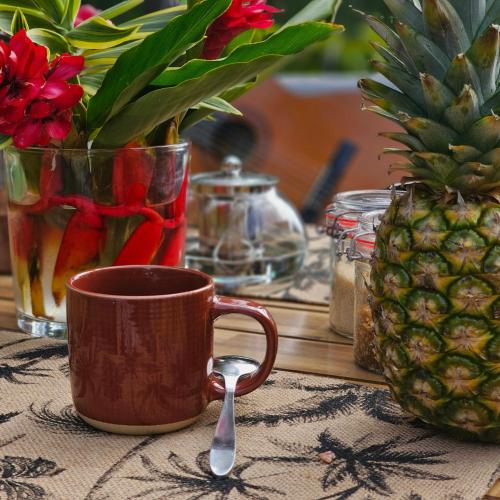 a coffee cup and a spoon on a table with a pineapple at o'Filao in Grand-Bourg