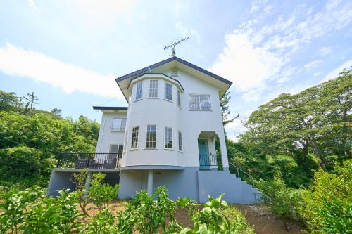 a white house on a hill with trees at Suite Villa Izukogen Mikanno-Hanasaku-Shiroiie in Ito