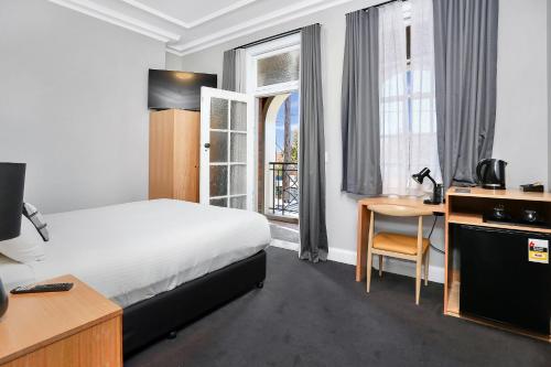 a hotel room with a bed and a desk and a window at Penshurst Hotel in Sydney
