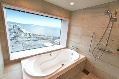 Odysis Suites Osaka Airport Hotel في إيزوميسانو: حوض استحمام في حمام مع نافذة كبيرة