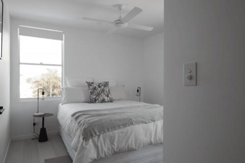 1 dormitorio blanco con 1 cama y ventilador de techo en Treasure on Trestles - Premium Holiday Home hosted by Holiday Management, en Casuarina