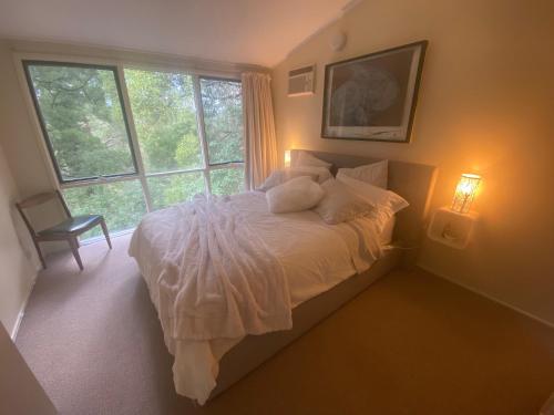 1 dormitorio con 1 cama con sábanas blancas y ventana en Sassafras Treehouse Private home in the Dandenong Ranges, Victoria, en Sassafras