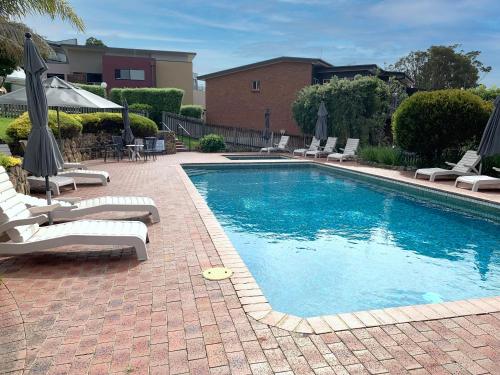 a swimming pool with lounge chairs and umbrellas next to at Pacific Heights in Merimbula