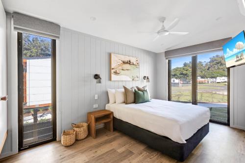 a bedroom with a large bed and large windows at Reflections Urunga - Holiday Park in Urunga