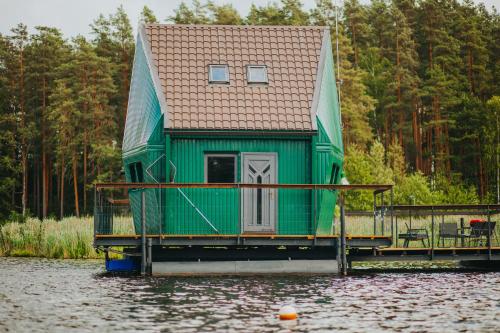 a green house on a dock on a body of water at Floating guest house Musters in Paķules