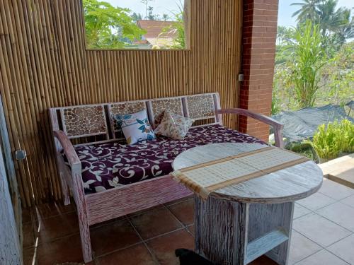 a bench with pillows on a porch with a table at Pondok isoke bunggalow in Banyuwangi