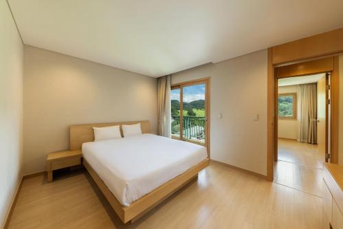 a bedroom with a white bed and a balcony at Oak Valley Resort Valley Village in Wonju
