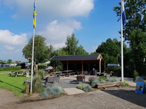 a pavilion with picnic tables and benches in a park at Camping Kleine Belterwijde, Wiede Lodge met uitzicht over het water in Belt-Schutsloot