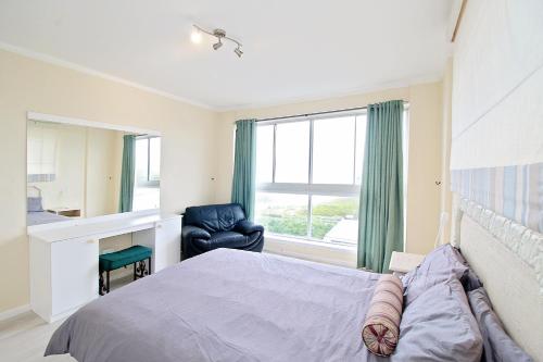 a bedroom with a bed and a chair and a window at Blouberg heights in Cape Town