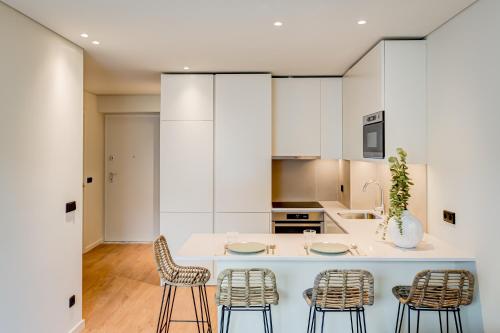 波尔图Blissful Suites Porto by gaiarooms的一个带白色橱柜的厨房和一个带椅子的岛屿