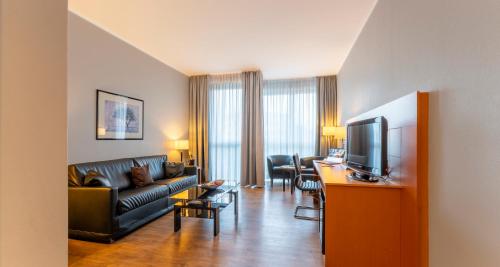 a living room with a couch and a television and a table at PLAZA Premium Köln in Cologne