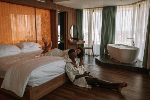 two women sitting on a bed in a bedroom with a tub at Bellerive Hoi An Resort and Spa in Hoi An