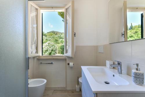 ein weißes Bad mit einem Waschbecken und einem Fenster in der Unterkunft Casa Camilla in Procchio