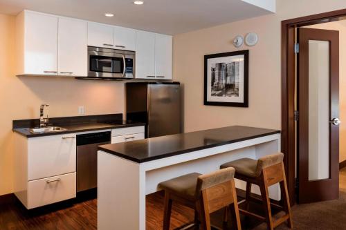 a kitchen with white cabinets and a bar with stools at Four Points by Sheraton Kelowna Airport in Kelowna